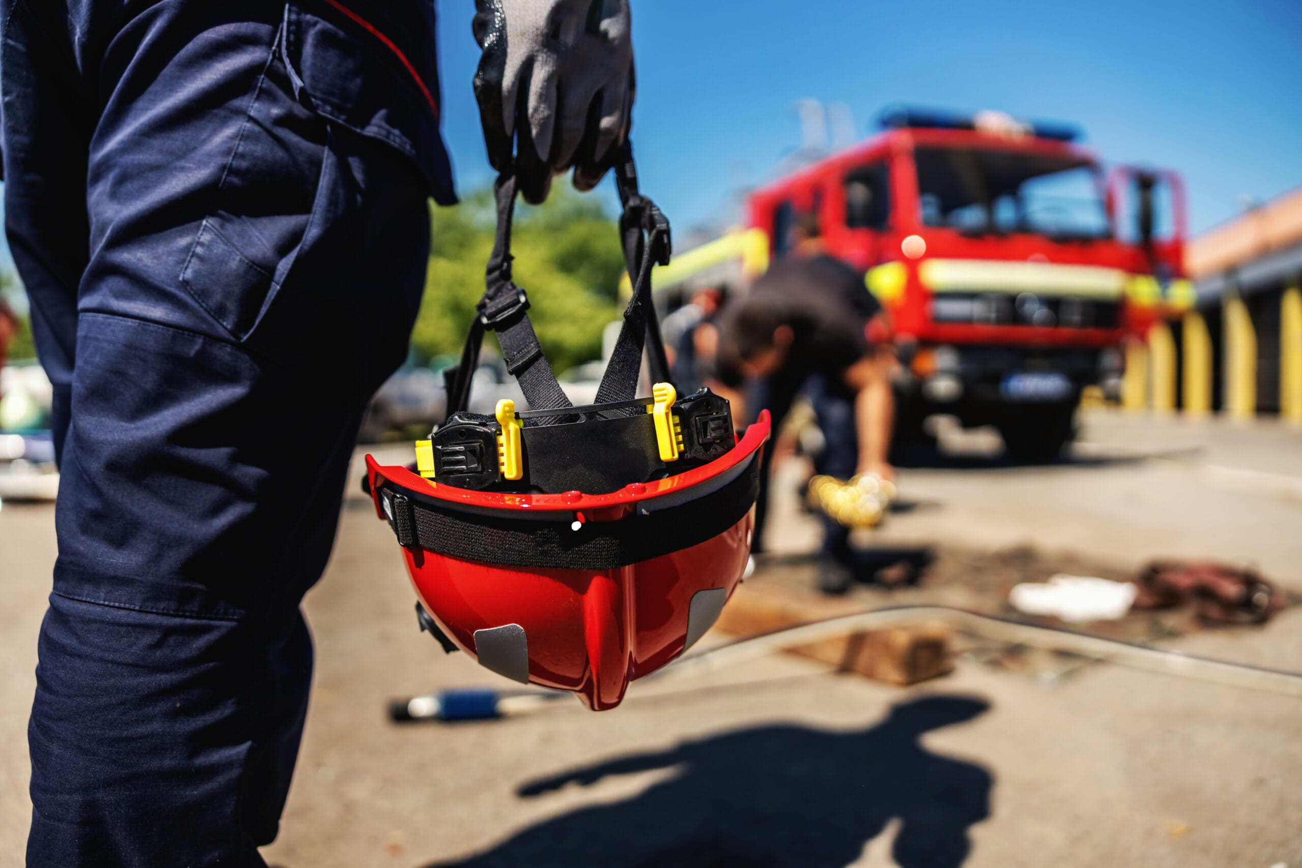 Closeup of firefighter holding his helmet and walking towards fire truck.